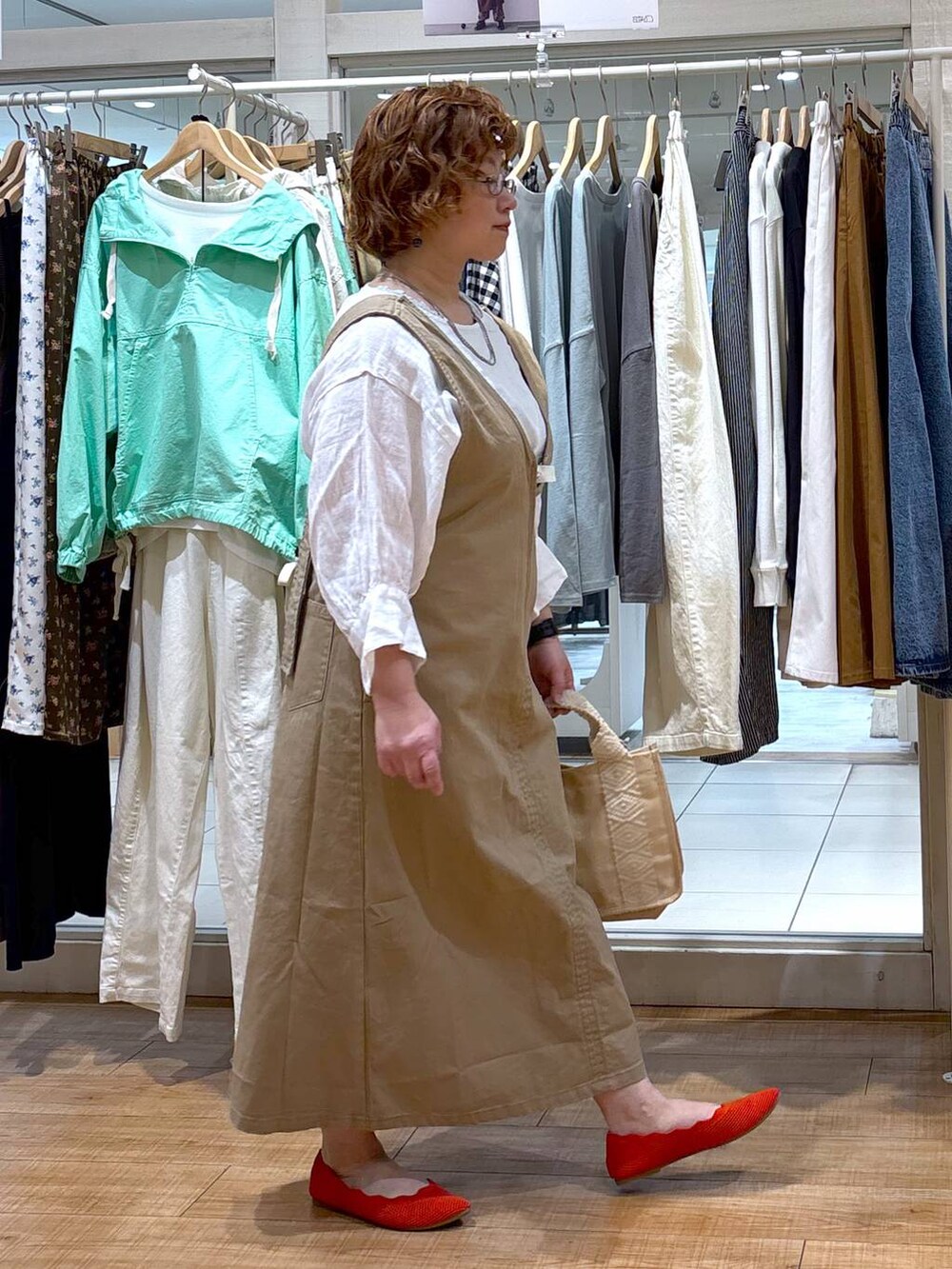 ベージュ系のジャンパースカート、ホワイト系のシャツ/ブラウス、グリーン系のタンクトップを着用したレディースの春コーディネートの3枚目の写真