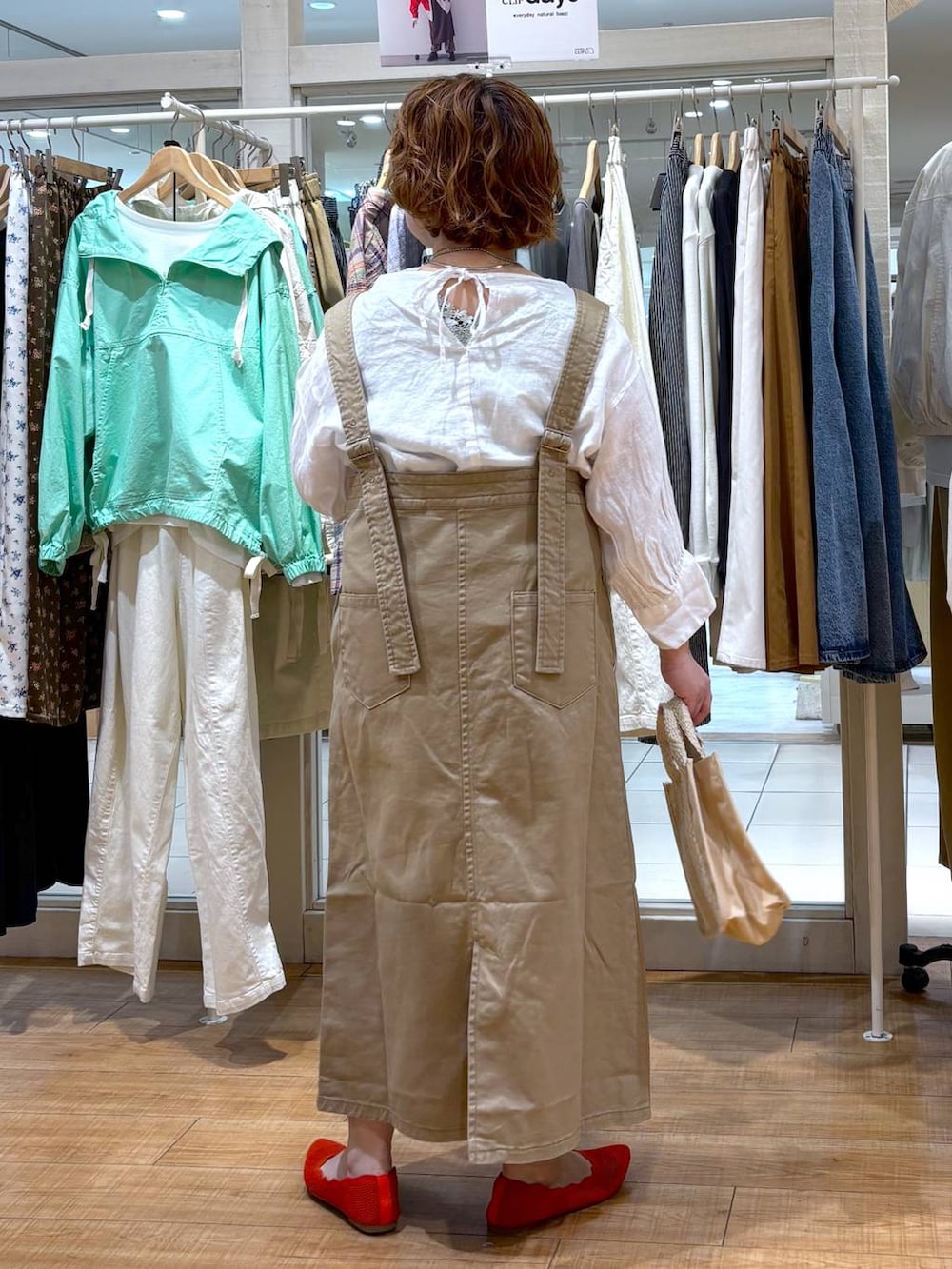 ベージュ系のジャンパースカート、ホワイト系のシャツ/ブラウス、グリーン系のタンクトップを着用したレディースの春コーディネートの4枚目の写真