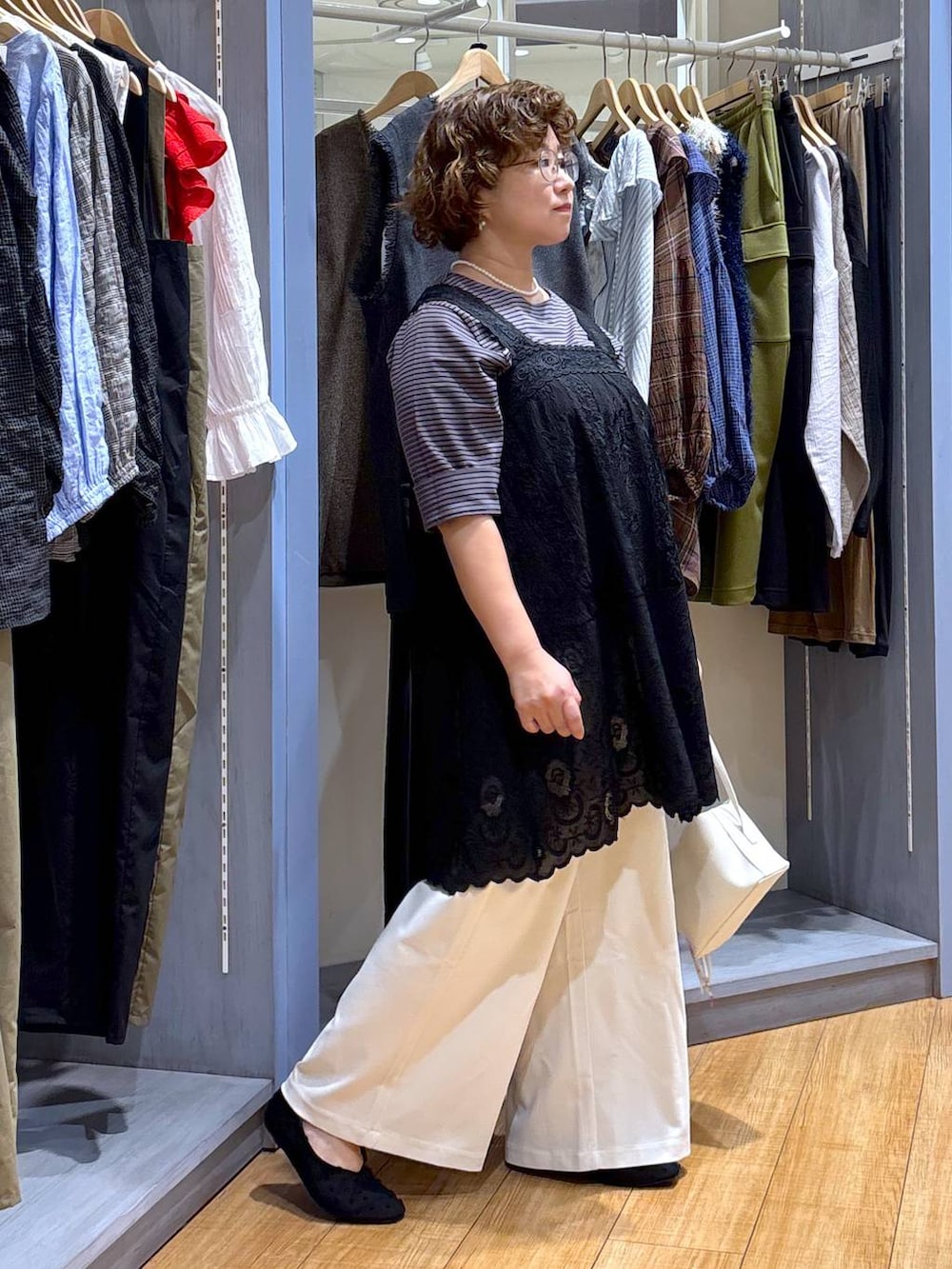 ホワイト系のショルダーバッグ、ブラック系のチュニック、ブラック系のパンプスを着用したレディースの夏コーディネートの3枚目の写真