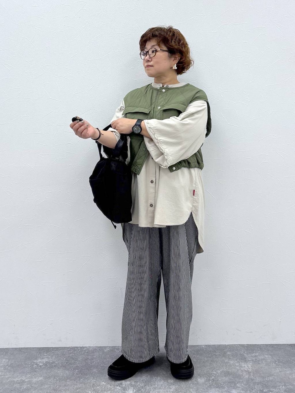 グリーン系のベスト、ブラック系のショルダーバッグ、ブラック系のその他パンツを着用したレディースの秋コーディネートの3枚目の写真