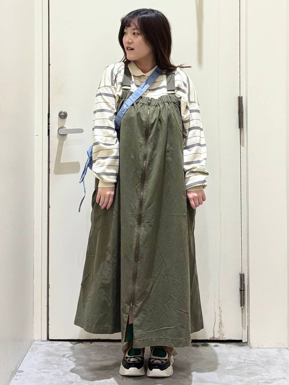 グリーン系のジャンパースカート、その他のスニーカー、ブルー系のショルダーバッグを着用したレディースの冬コーディネートの3枚目の写真