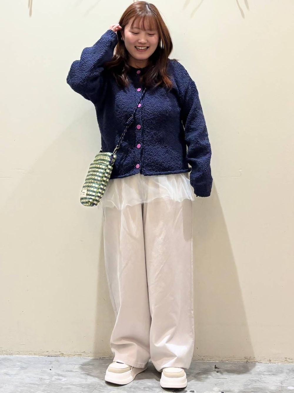 グリーン系のショルダーバッグ、ブルー系のニット/セーター、ベージュ系のチノパンツを着用したレディースの冬コーディネートの2枚目の写真