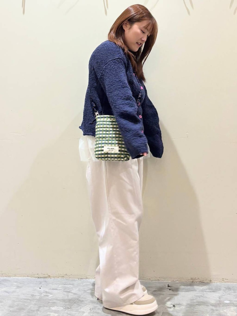 グリーン系のショルダーバッグ、ブルー系のニット/セーター、ベージュ系のチノパンツを着用したレディースの冬コーディネートの5枚目の写真