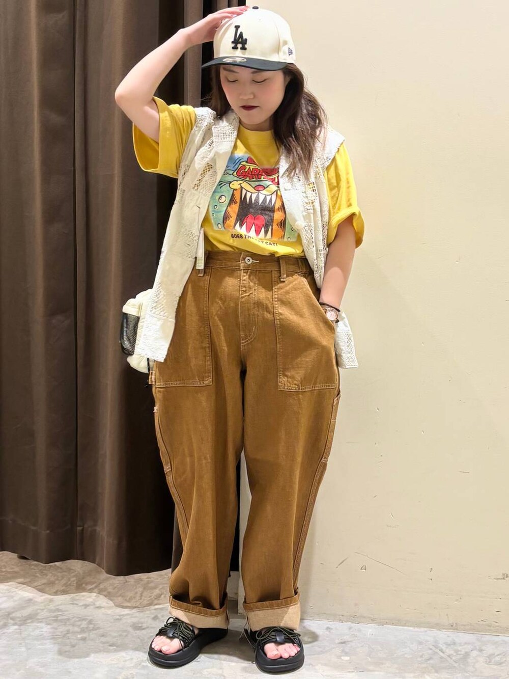 ベージュ系のベスト、ブラウン系のデニムパンツ、ブラック系のサンダルを着用したレディースの夏コーディネートの2枚目の写真
