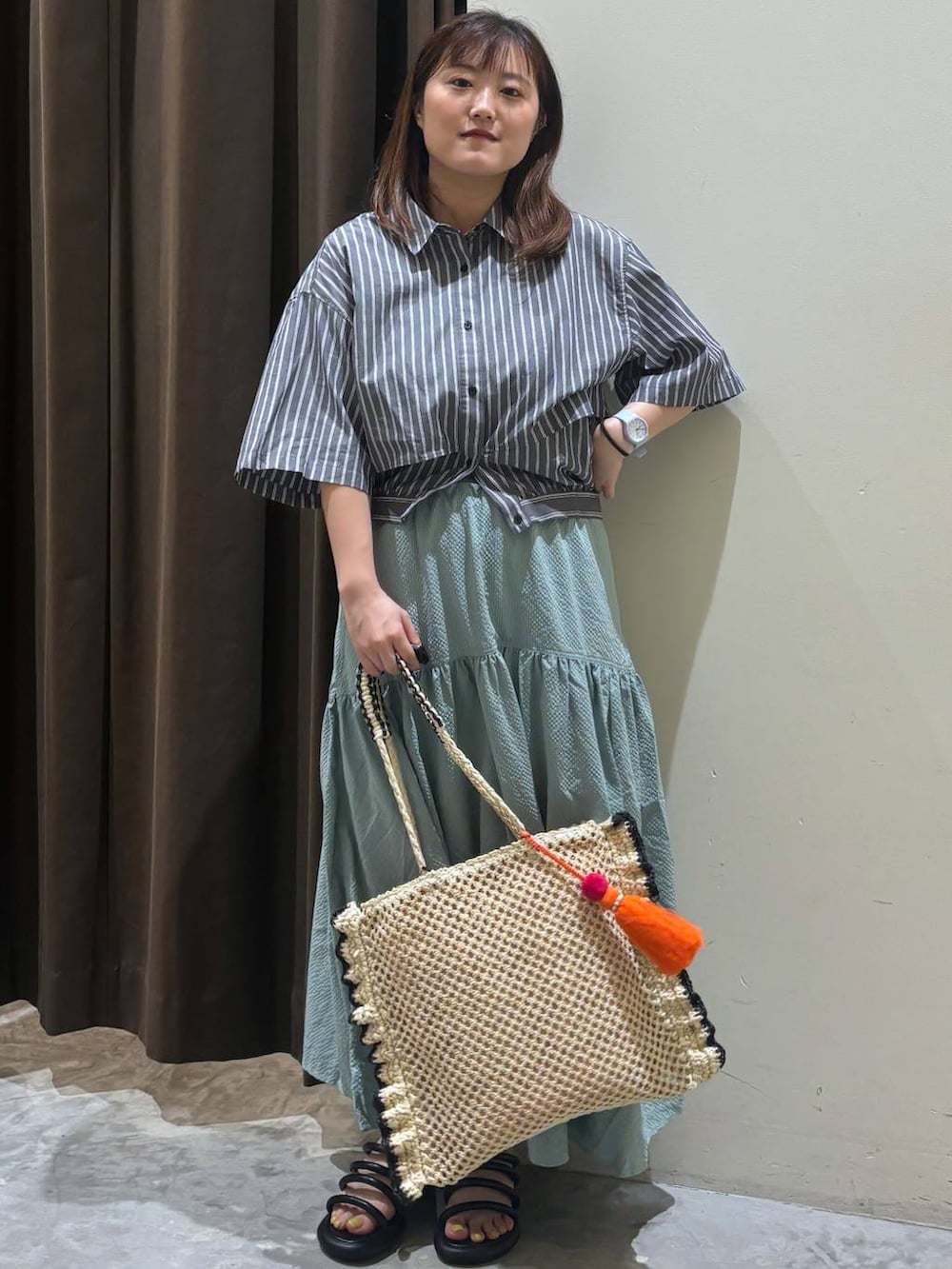 ブラック系のサンダル、グリーン系のスカート、ベージュ系のトートバッグを着用したレディースの夏コーディネートの2枚目の写真