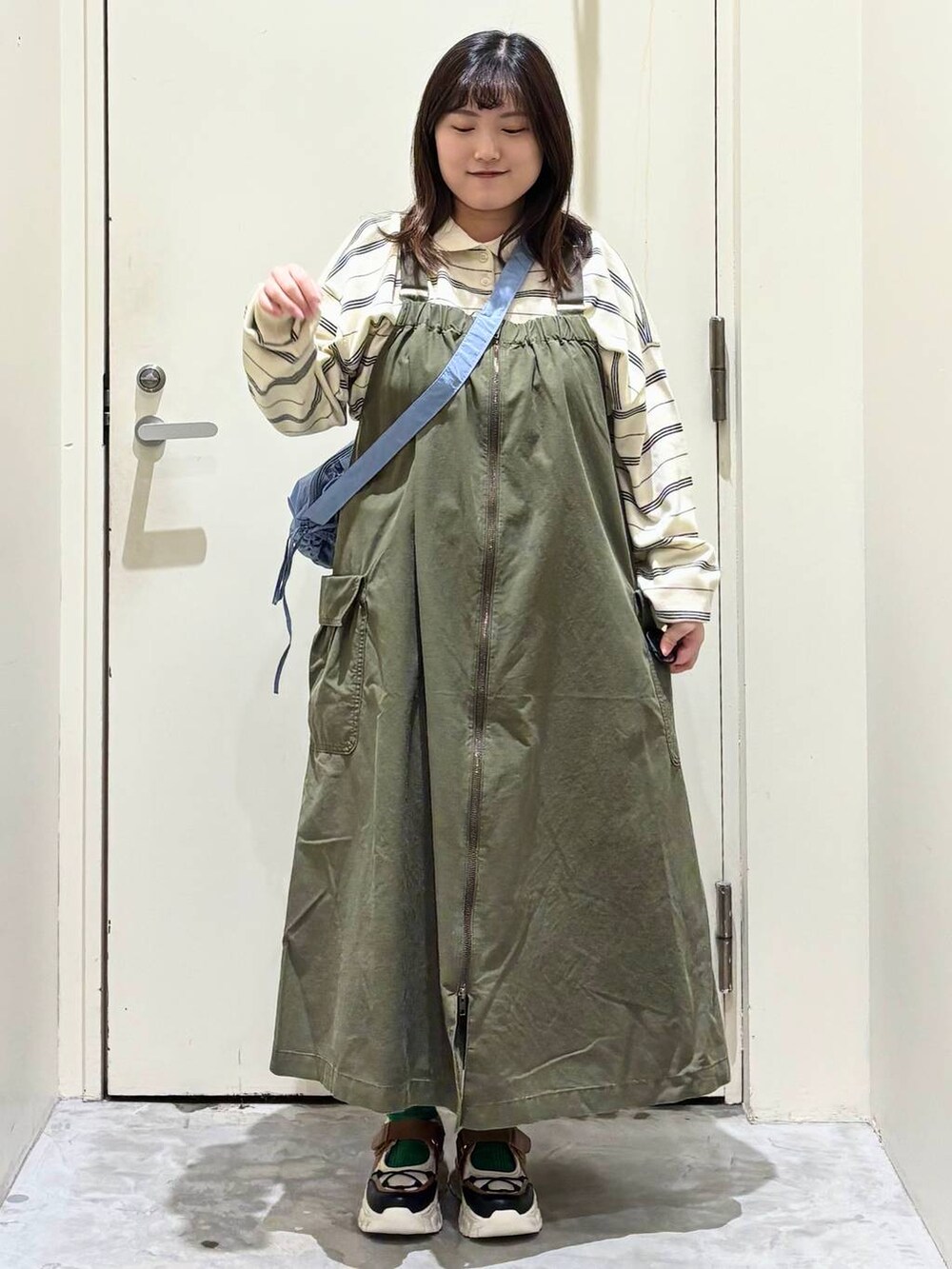 グリーン系のジャンパースカート、その他のスニーカー、ブルー系のショルダーバッグを着用したレディースの冬コーディネートの2枚目の写真