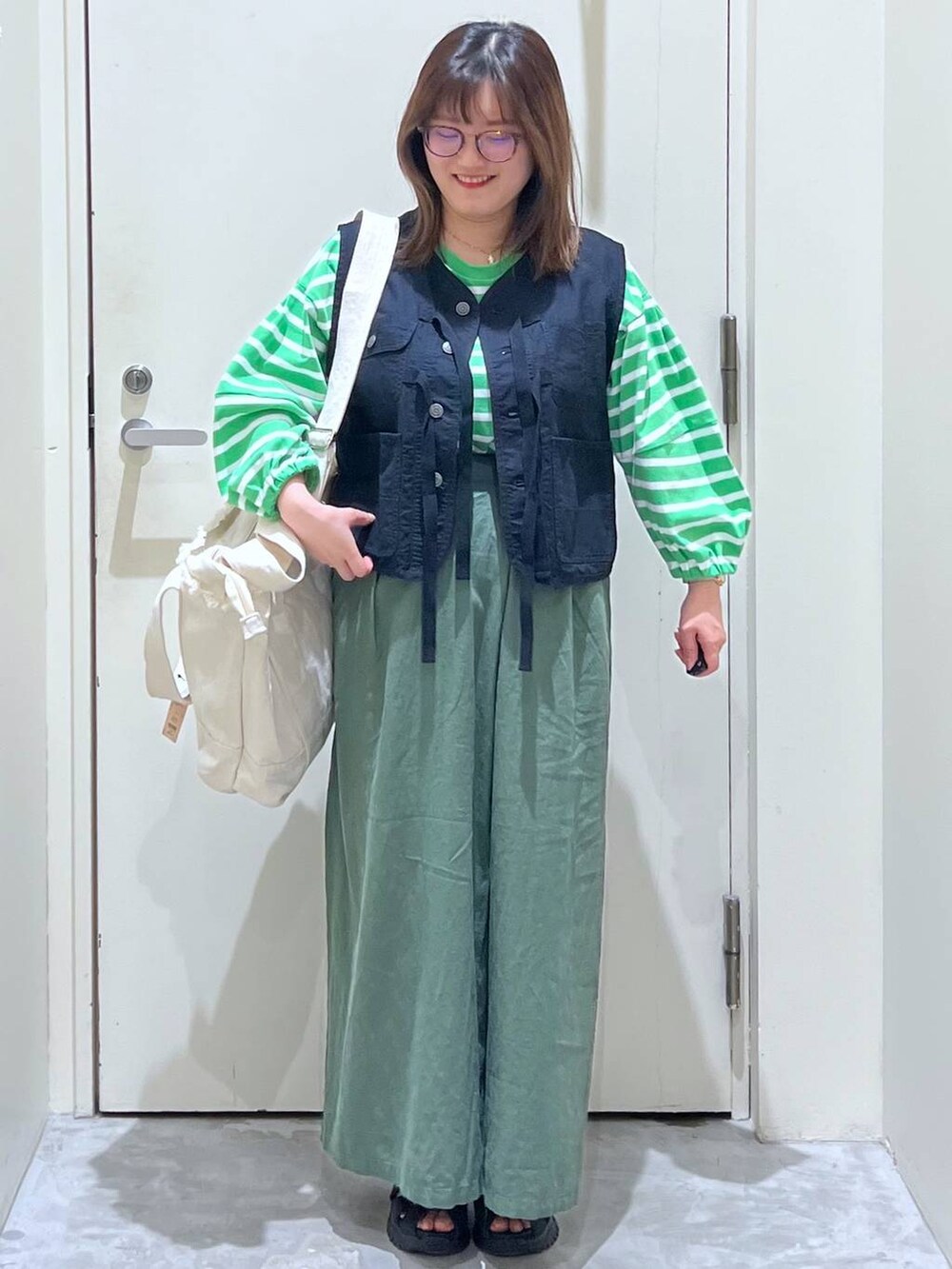 ベージュ系のショルダーバッグ、ブラック系のサンダル、ブラック系のベストを着用したレディースの春コーディネートの2枚目の写真