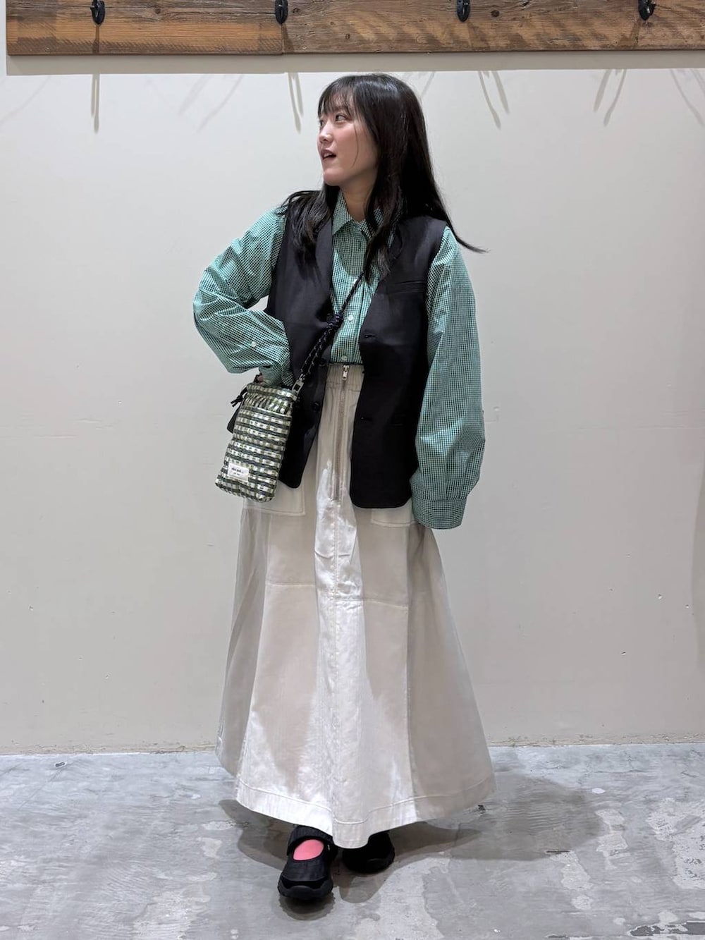 グリーン系のショルダーバッグ、ブラック系のベスト、ブラック系のバレエシューズを着用したレディースの春コーディネートの2枚目の写真