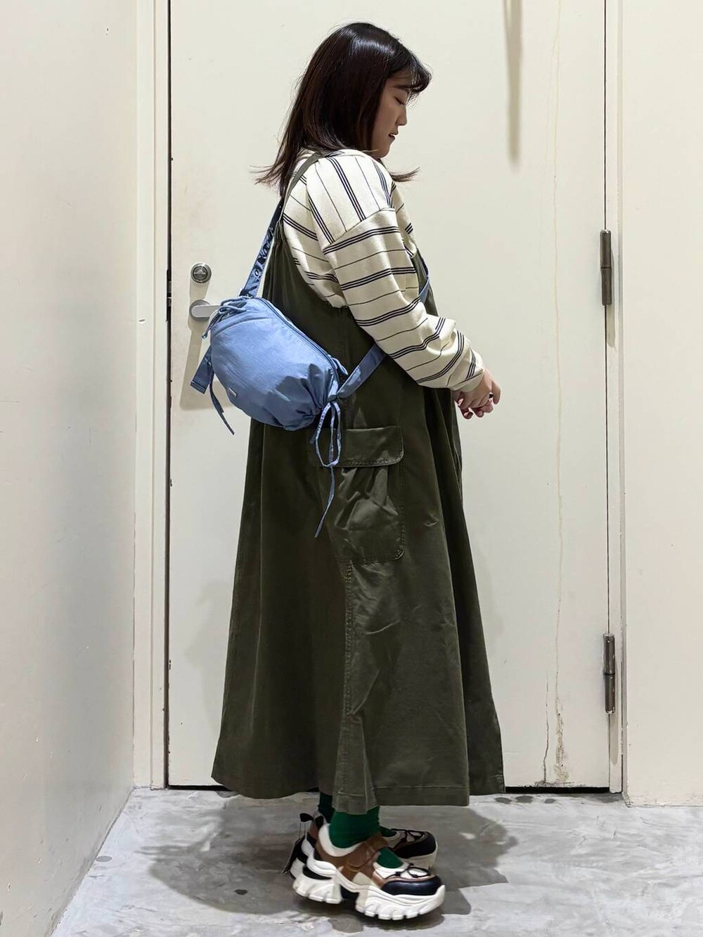 グリーン系のジャンパースカート、その他のスニーカー、ブルー系のショルダーバッグを着用したレディースの冬コーディネートの6枚目の写真