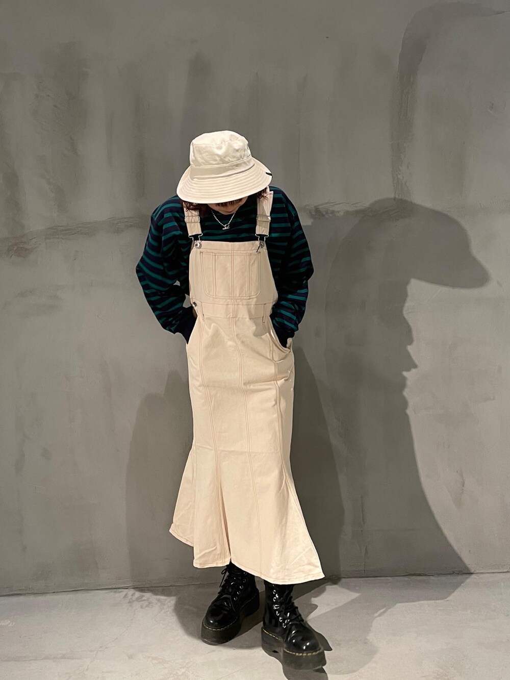 ブルー系のTシャツ/カットソー、ホワイト系のジャンパースカート、ブラック系のブーツを着用したレディースの春コーディネートの2枚目の写真