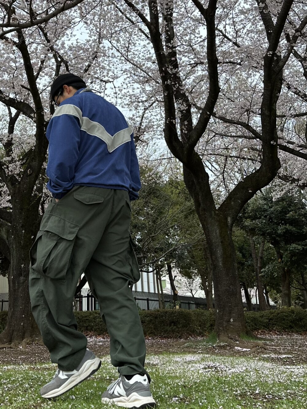 グリーン系のカーゴパンツ、ブルー系のナイロンジャケット、グレー系のスニーカーを着用したメンズの春コーディネートの2枚目の写真