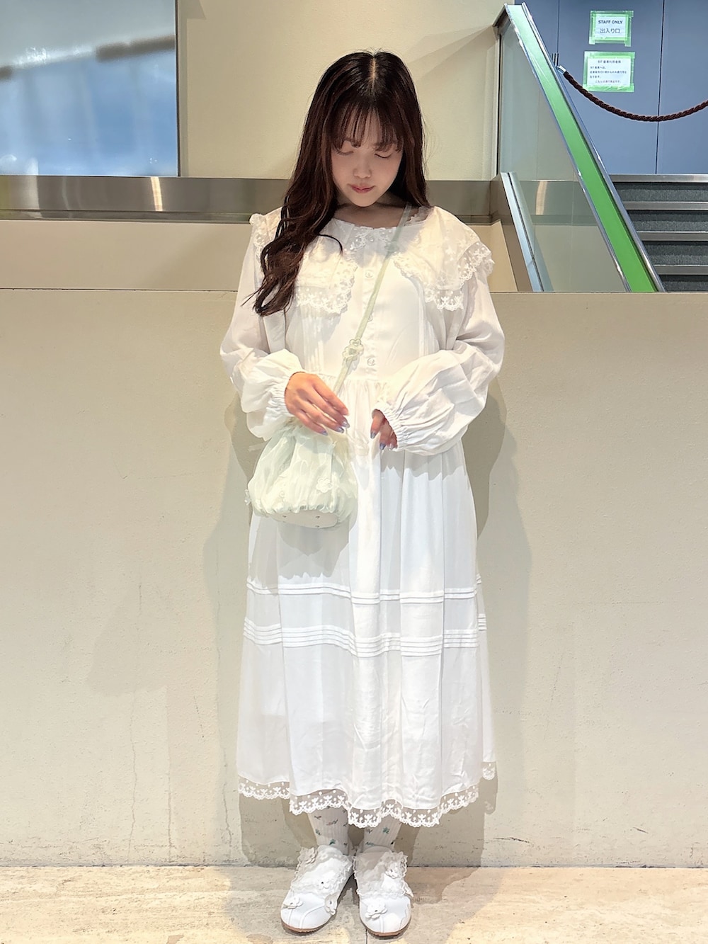 グリーン系のハンドバッグ、ホワイト系のスニーカー、ホワイト系のワンピースを着用したレディースの冬コーディネートの3枚目の写真