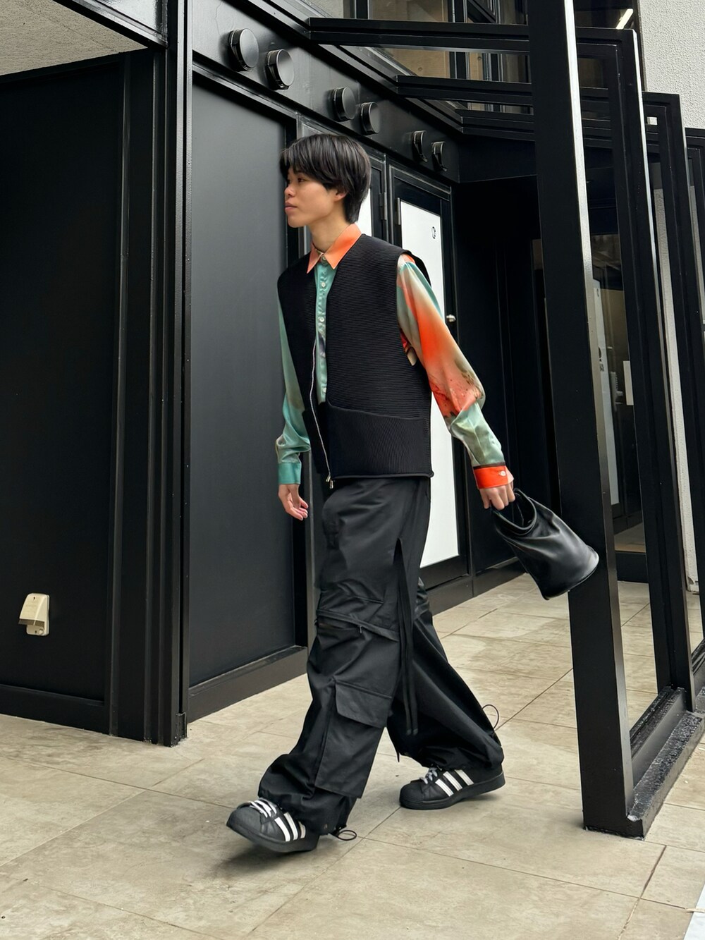 オレンジ系のシャツ/ブラウス、ブラック系のカーゴパンツ、ホワイト系のスニーカーを着用したメンズの春コーディネートの2枚目の写真