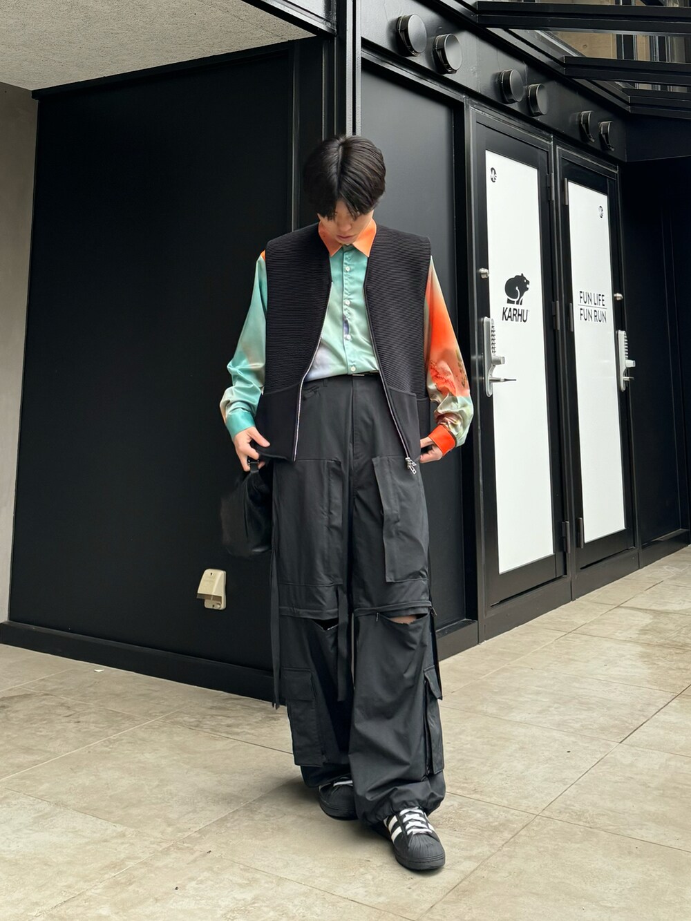 オレンジ系のシャツ/ブラウス、ブラック系のカーゴパンツ、ホワイト系のスニーカーを着用したメンズの春コーディネートの3枚目の写真