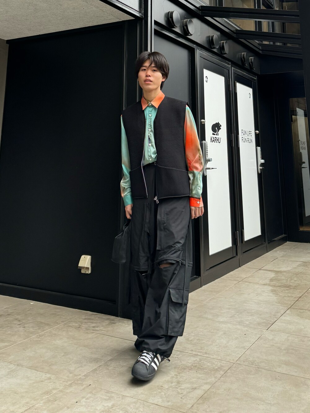 オレンジ系のシャツ/ブラウス、ブラック系のカーゴパンツ、ホワイト系のスニーカーを着用したメンズの春コーディネートの5枚目の写真