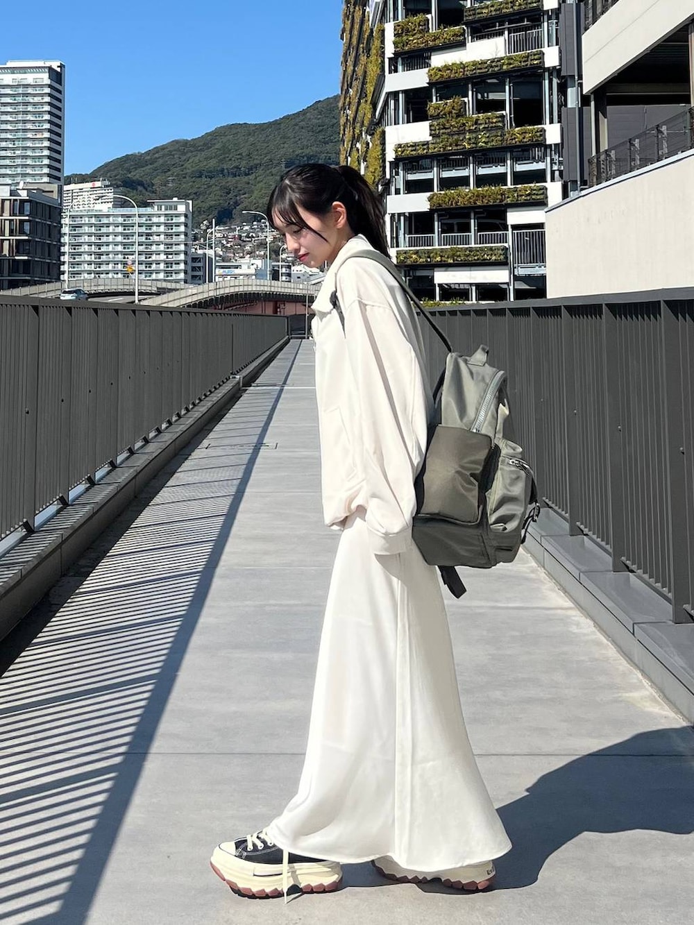 ブラック系のスニーカー、グリーン系のバックパック/リュック、ホワイト系のスカートを着用したレディースの春コーディネートの2枚目の写真