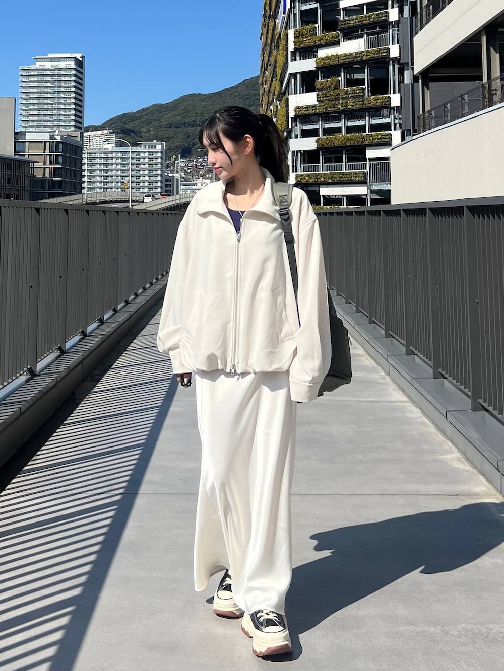 ブラック系のスニーカー、グリーン系のバックパック/リュック、ホワイト系のスカートを着用したレディースの春コーディネートの5枚目の写真