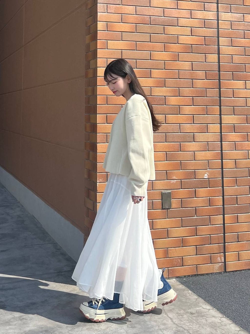 ブルー系のスニーカー、ホワイト系のカーディガン/ボレロ、ホワイト系のスカートを着用したレディースの春コーディネートの2枚目の写真