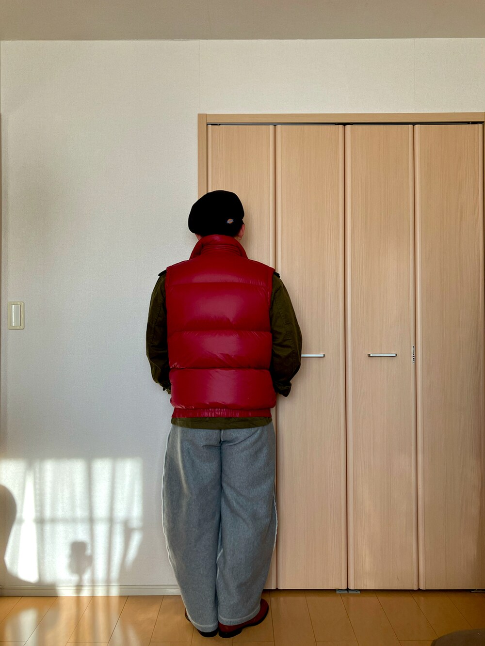 グレー系のスウェットパンツ、レッド系のダウンベスト、ブラウン系のローファーを着用したメンズの冬コーディネートの2枚目の写真