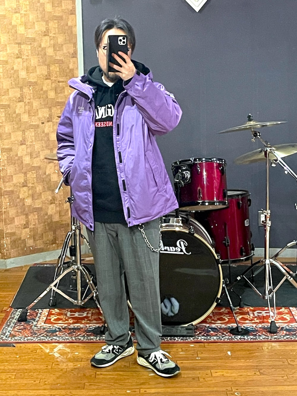 パープル系のマウンテンパーカー、ブラック系のパーカー、グレー系のスラックスを着用したメンズの春コーディネートの4枚目の写真