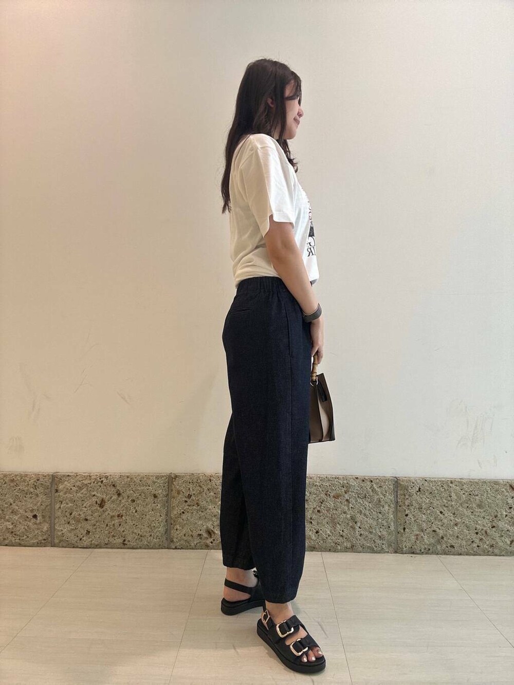 ブラック系のショルダーバッグ、ブラック系のサンダル、ホワイト系のTシャツ/カットソーを着用したレディースの夏コーディネートの2枚目の写真