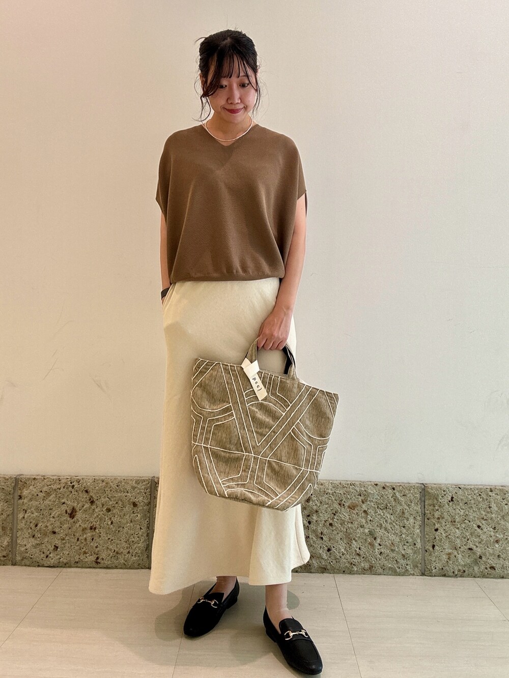 イエロー系のニット/セーター、ホワイト系のスカート、ブラック系のパンプスを着用したレディースの秋コーディネートの2枚目の写真