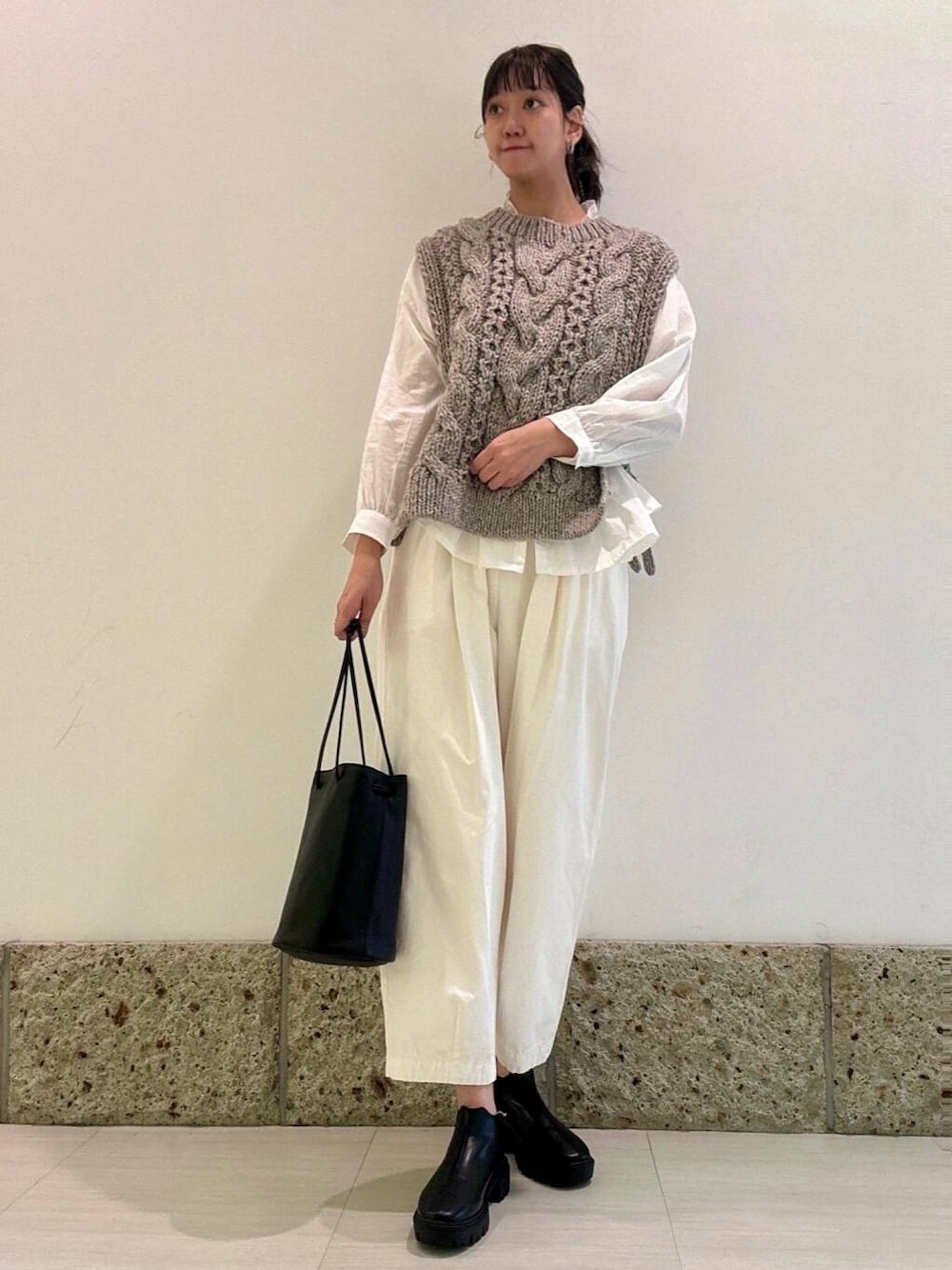 グレー系のニット/セーター、ブラック系のショルダーバッグ、ブラック系のブーツを着用したレディースの秋コーディネートの2枚目の写真