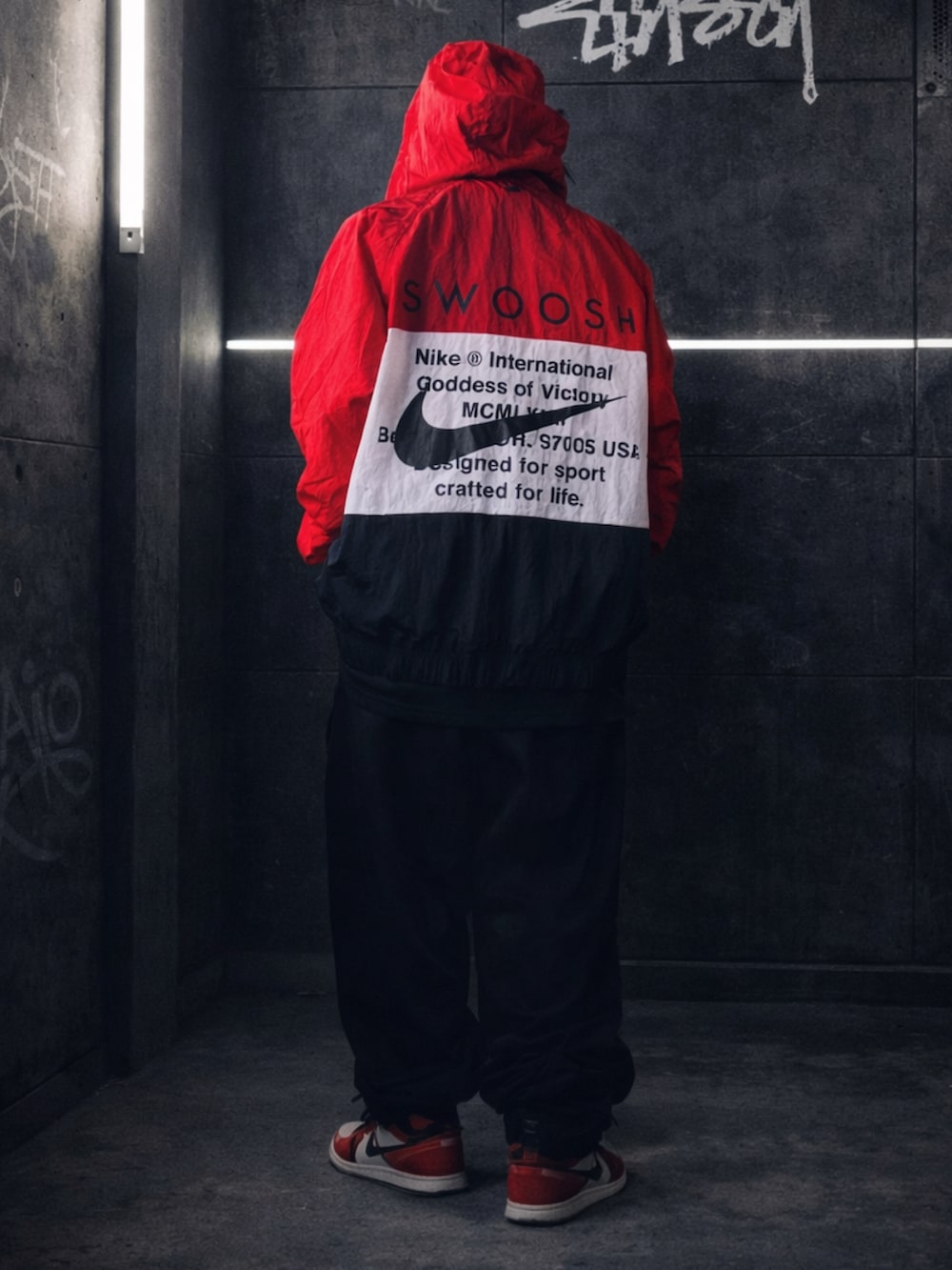 レッド系のナイロンジャケット、ブラック系のTシャツ/カットソー、ブラック系のスウェットパンツを着用したメンズの冬コーディネートの2枚目の写真