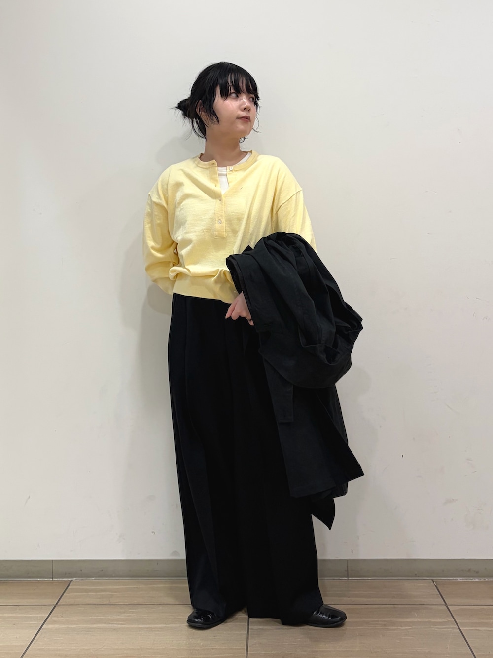 ブラック系のステンカラーコート、イエロー系のニット/セーター、ブラック系のその他パンツを着用したレディースの冬コーディネートの2枚目の写真