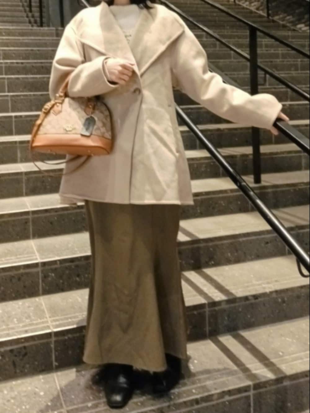 ブラウン系のボストンバッグ、ベージュ系のダッフルコート、ブラウン系のスカートを着用したレディースの春コーディネートの3枚目の写真