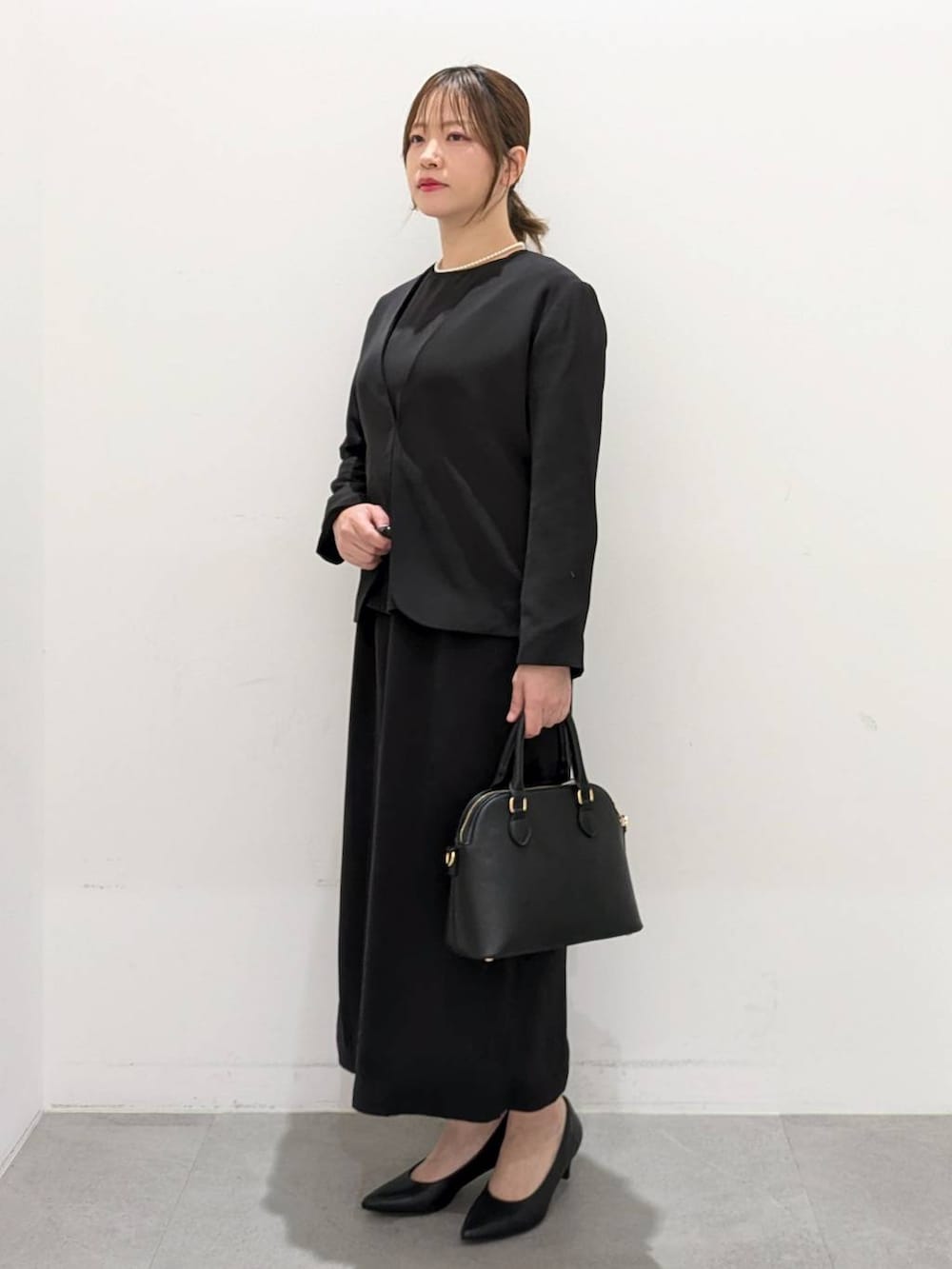 ブラック系のスーツジャケット、ブラック系のワンピース、ブラック系のパンプスを着用したレディースの春コーディネートの3枚目の写真
