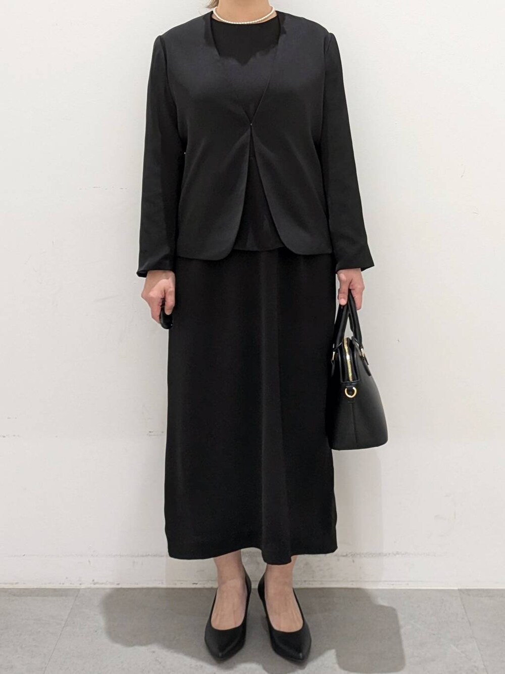 ブラック系のスーツジャケット、ブラック系のワンピース、ブラック系のパンプスを着用したレディースの春コーディネートの6枚目の写真