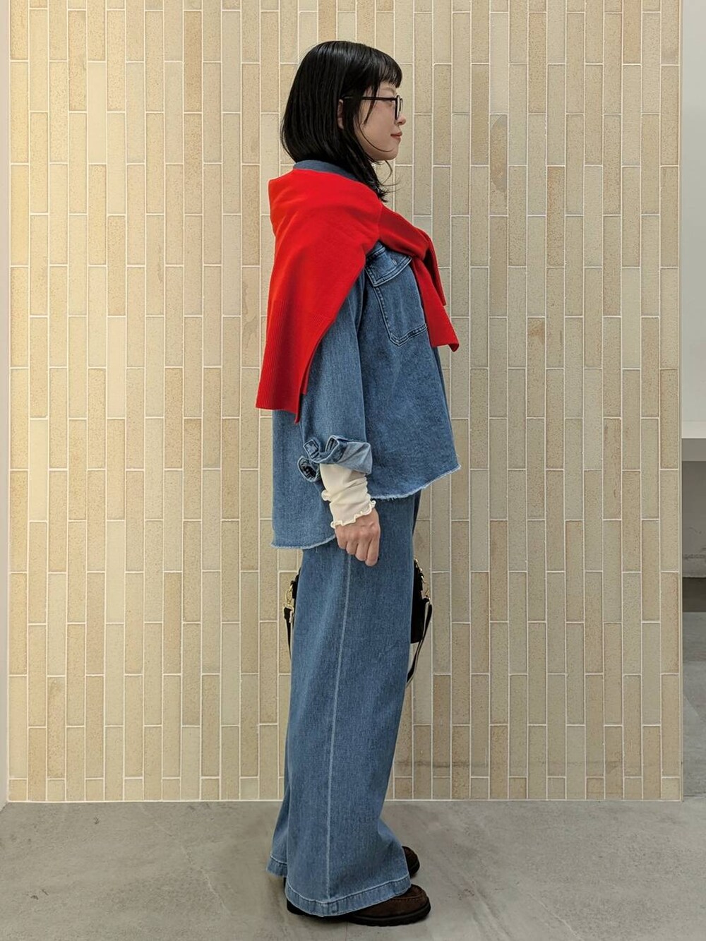 レッド系のニット/セーター、ブラック系のハンドバッグ、ブルー系のデニムパンツを着用したレディースの秋コーディネートの5枚目の写真