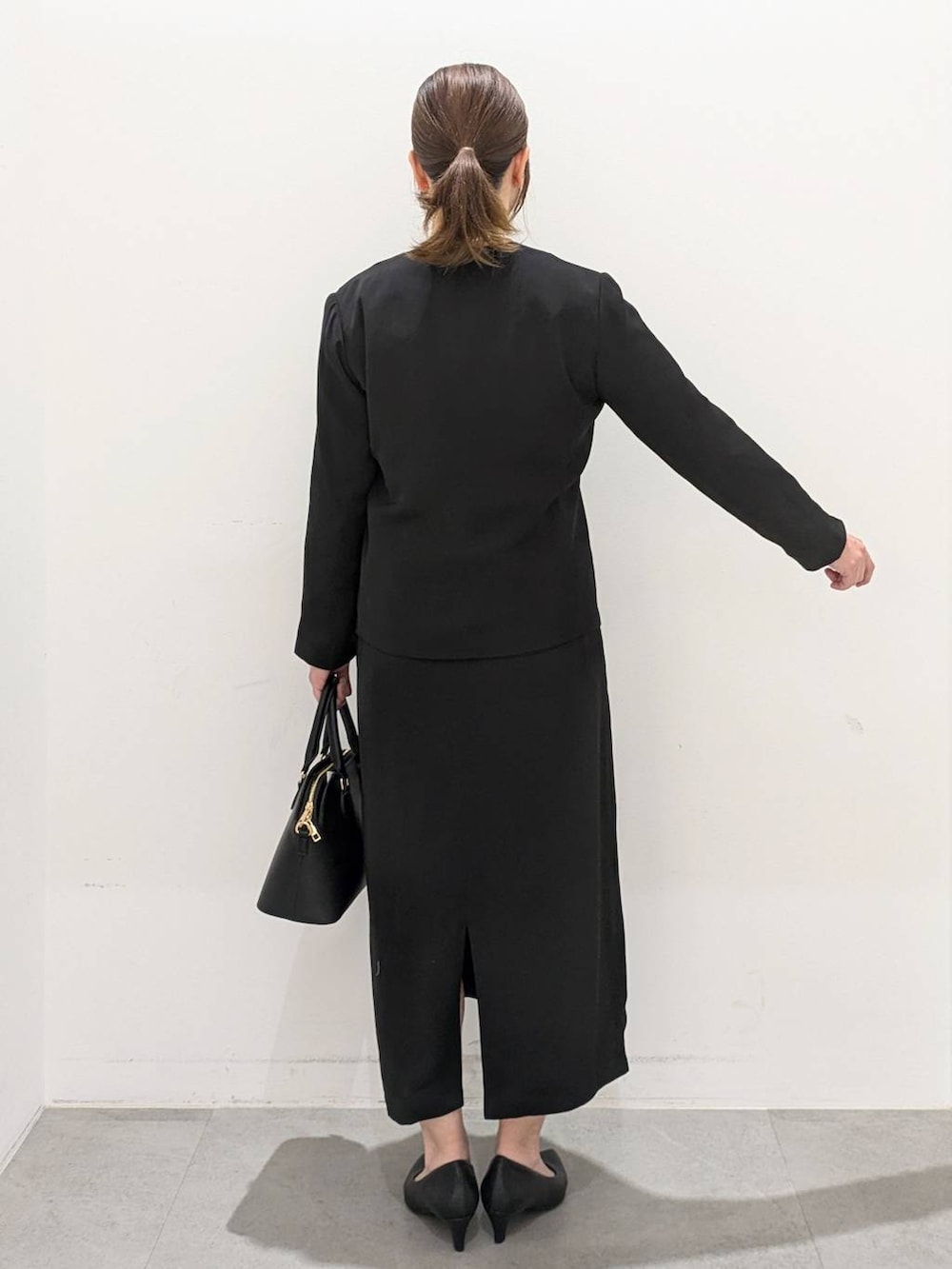 ブラック系のスーツジャケット、ブラック系のワンピース、ブラック系のパンプスを着用したレディースの春コーディネートの4枚目の写真