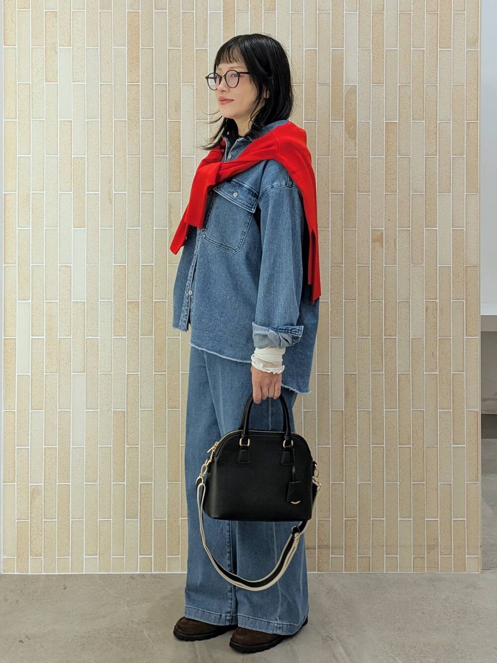 レッド系のニット/セーター、ブラック系のハンドバッグ、ブルー系のデニムパンツを着用したレディースの秋コーディネートの3枚目の写真