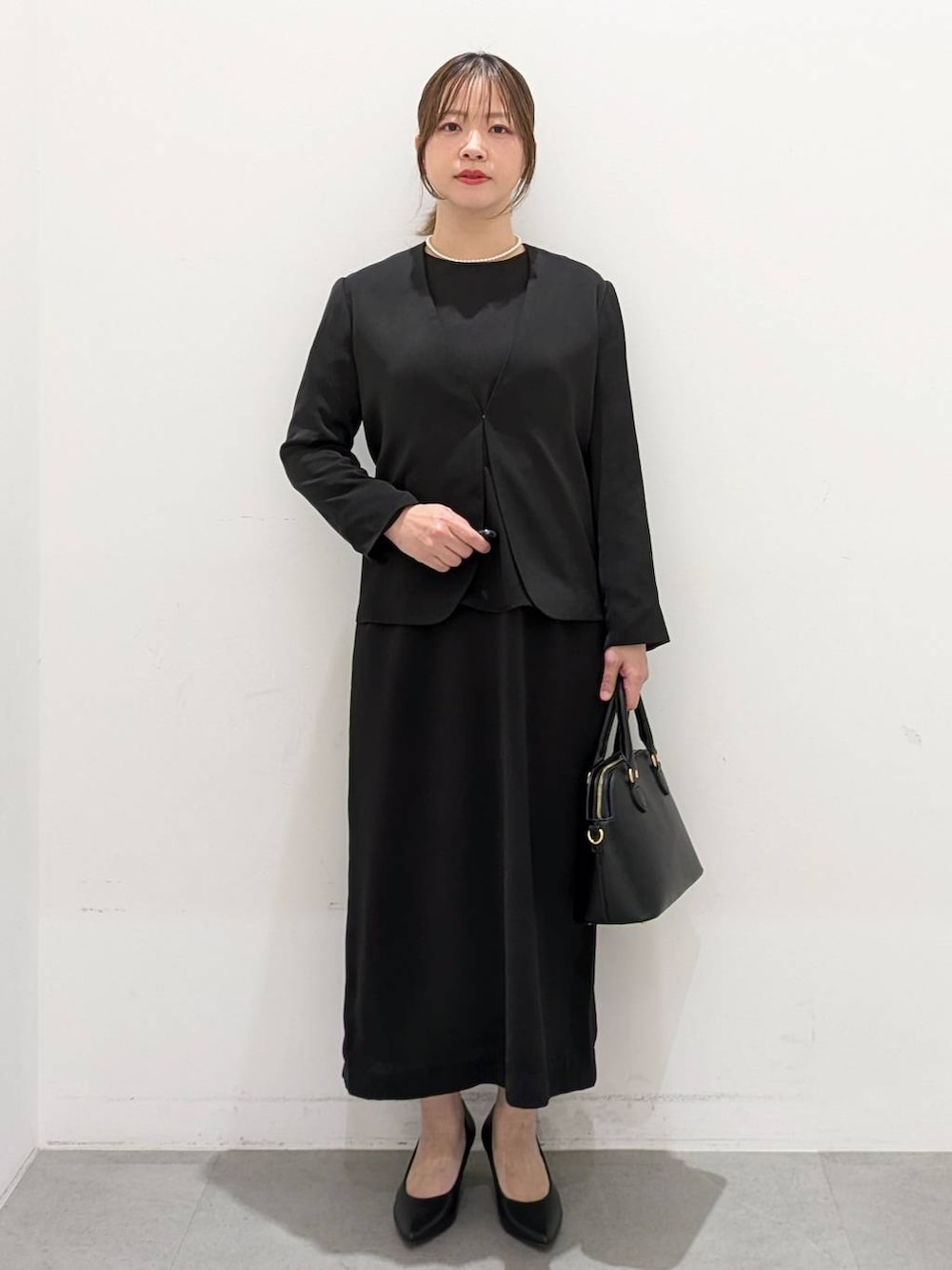 ブラック系のスーツジャケット、ブラック系のワンピース、ブラック系のパンプスを着用したレディースの春コーディネートの2枚目の写真
