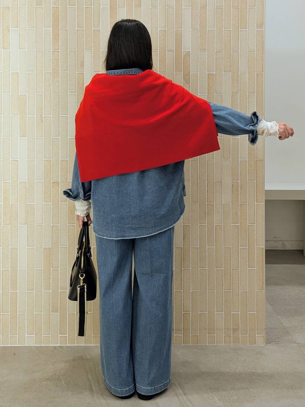 レッド系のニット/セーター、ブラック系のハンドバッグ、ブルー系のデニムパンツを着用したレディースの秋コーディネートの4枚目の写真