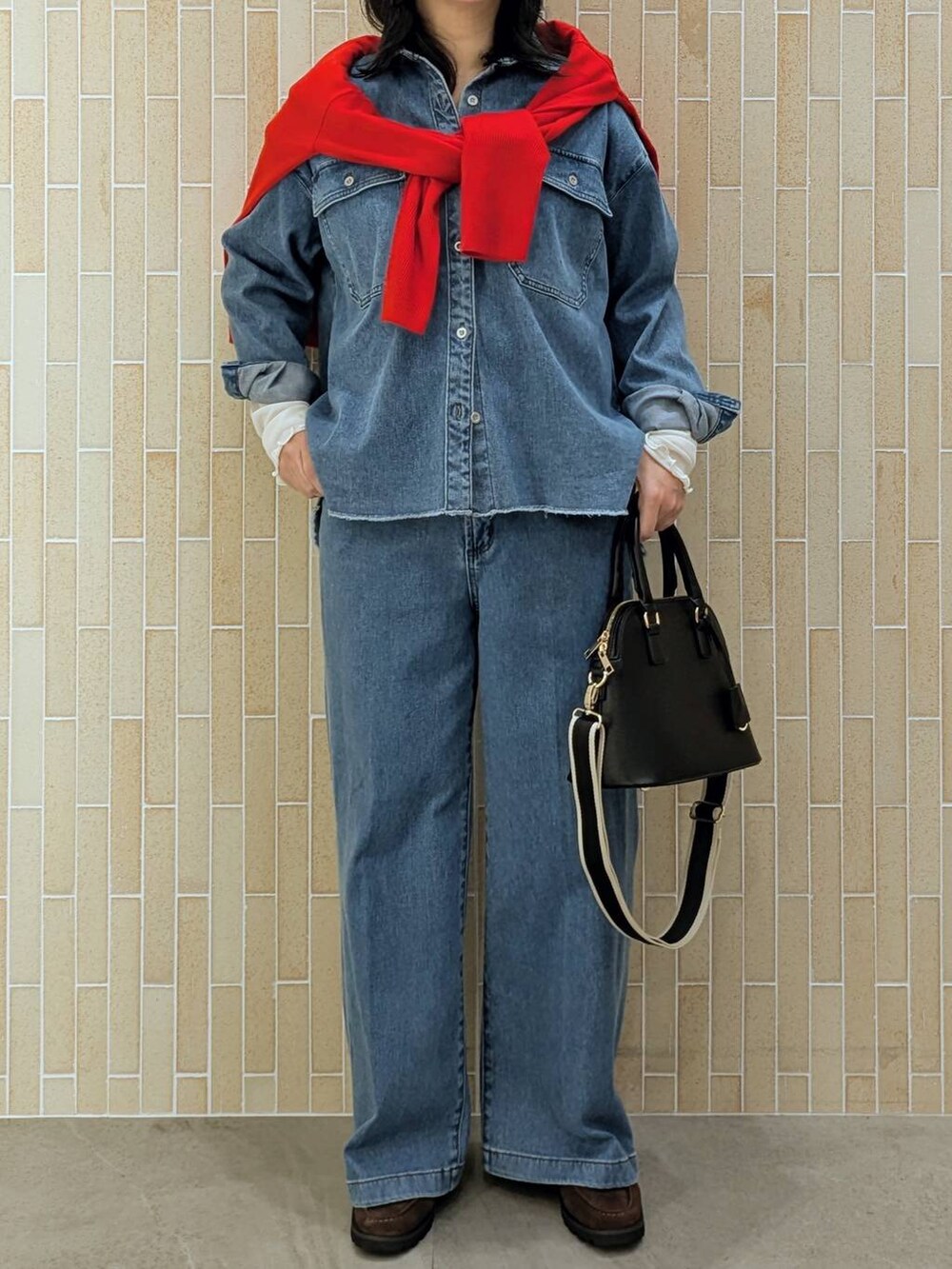 レッド系のニット/セーター、ブラック系のハンドバッグ、ブルー系のデニムパンツを着用したレディースの秋コーディネートの6枚目の写真