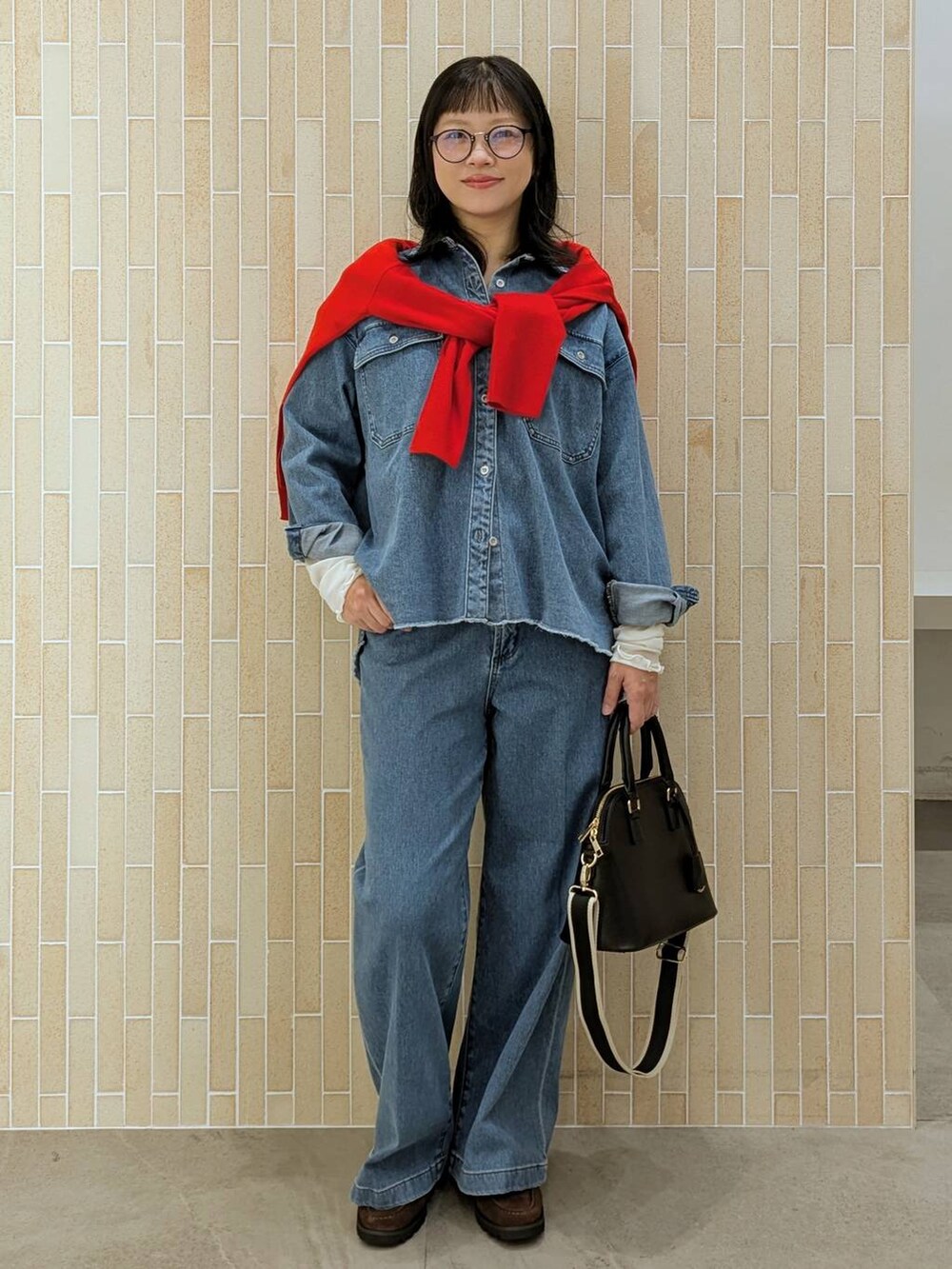 レッド系のニット/セーター、ブラック系のハンドバッグ、ブルー系のデニムパンツを着用したレディースの秋コーディネートの2枚目の写真