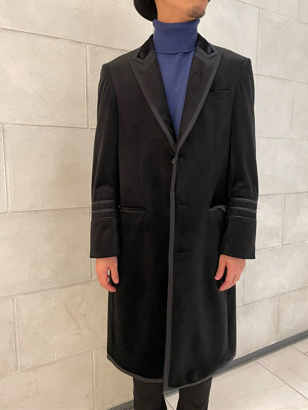 ブラック系のチェスターコート、ブルー系のニット/セーター、ブラック系のスニーカーを着用したメンズの冬コーディネートの3枚目の写真