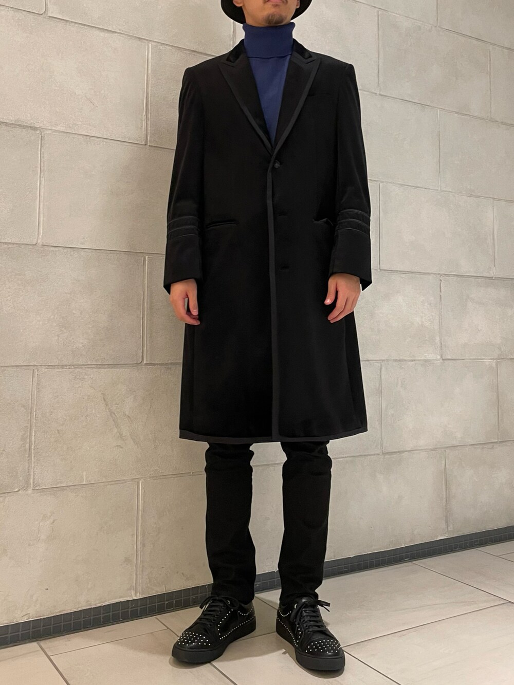 ブラック系のチェスターコート、ブルー系のニット/セーター、ブラック系のスニーカーを着用したメンズの冬コーディネートの2枚目の写真