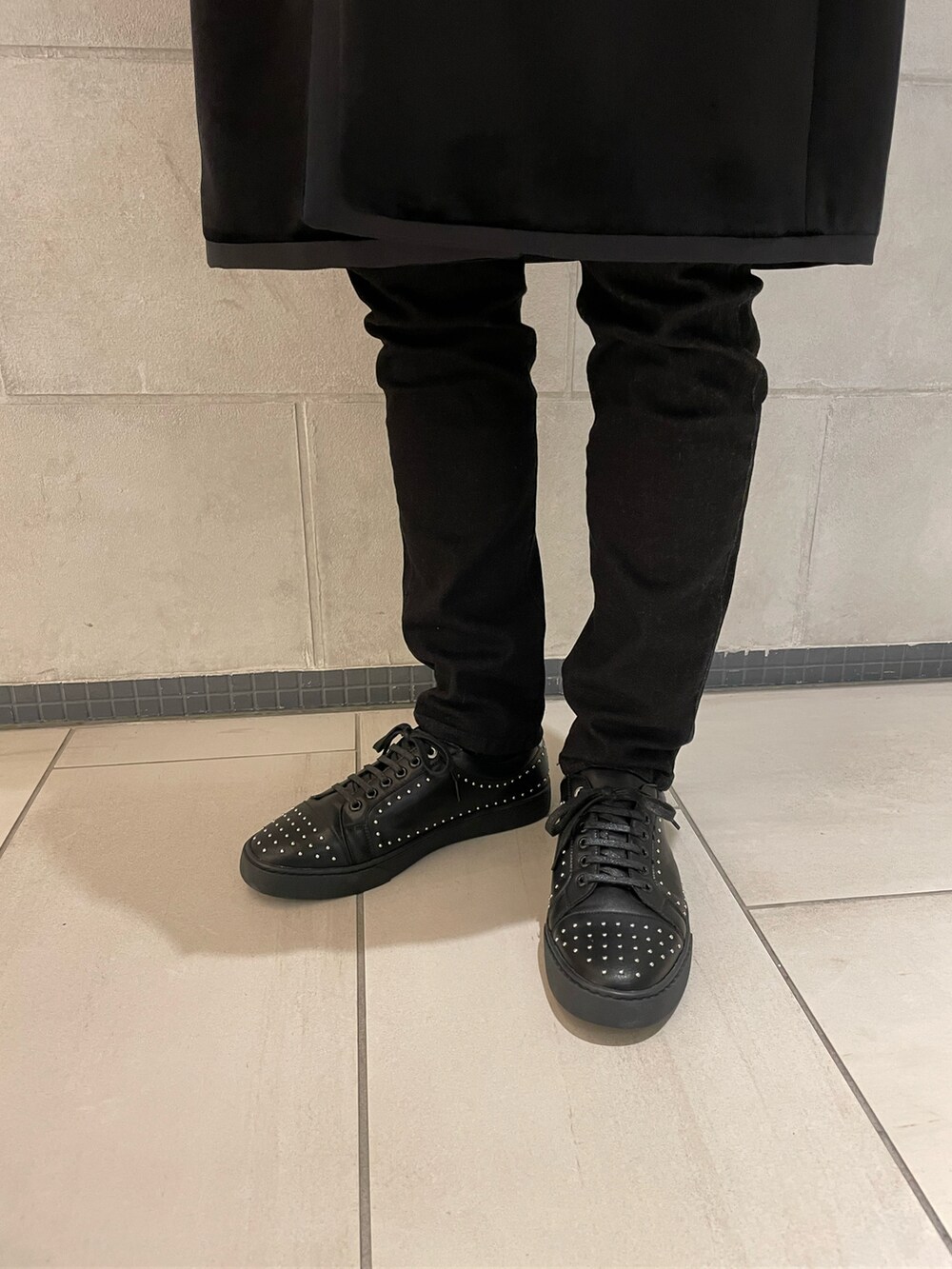 ブラック系のチェスターコート、ブルー系のニット/セーター、ブラック系のスニーカーを着用したメンズの冬コーディネートの4枚目の写真