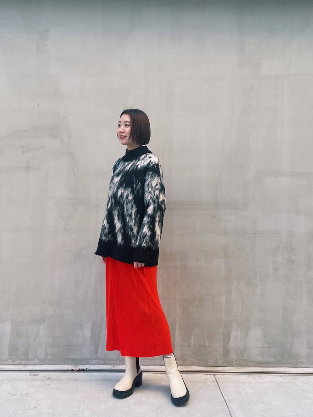 ブラック系のニット/セーター、オレンジ系のスカート、ホワイト系のブーツを着用したレディースの冬コーディネートの2枚目の写真