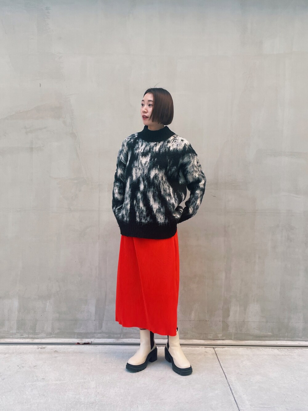 ブラック系のニット/セーター、オレンジ系のスカート、ホワイト系のブーツを着用したレディースの冬コーディネートの3枚目の写真