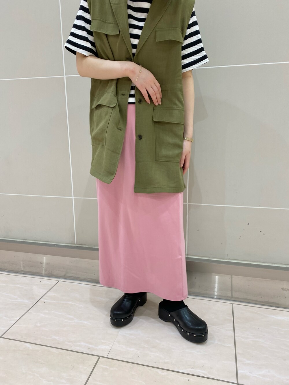 ブラック系のサンダル、ピンク系のスカート、グリーン系のベストを着用したレディースの春コーディネートの2枚目の写真
