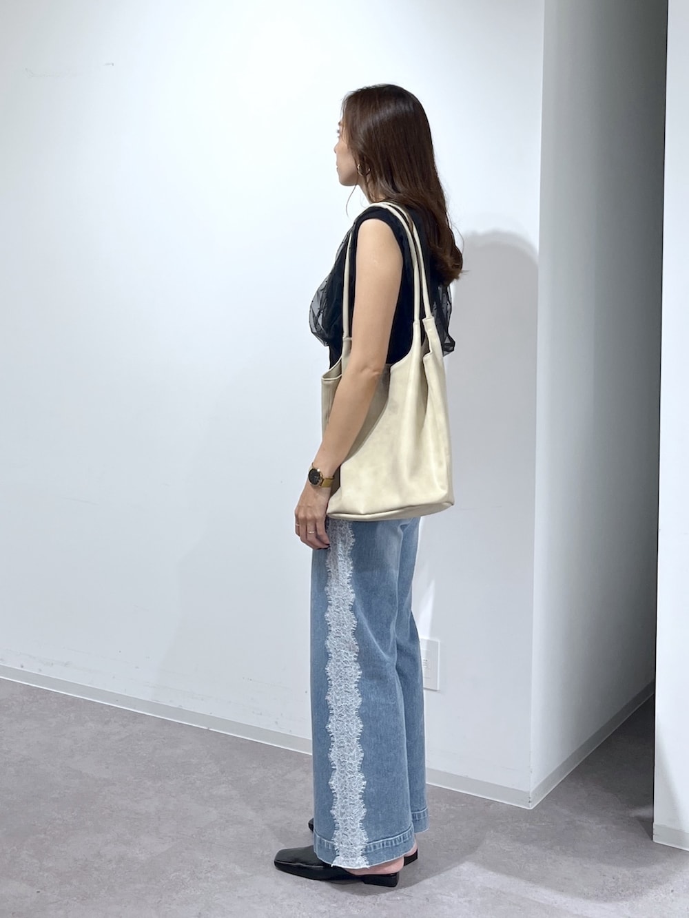 ブラック系のニット/セーター、ブルー系のデニムパンツ、ベージュ系のトートバッグを着用したレディースの夏コーディネートの5枚目の写真