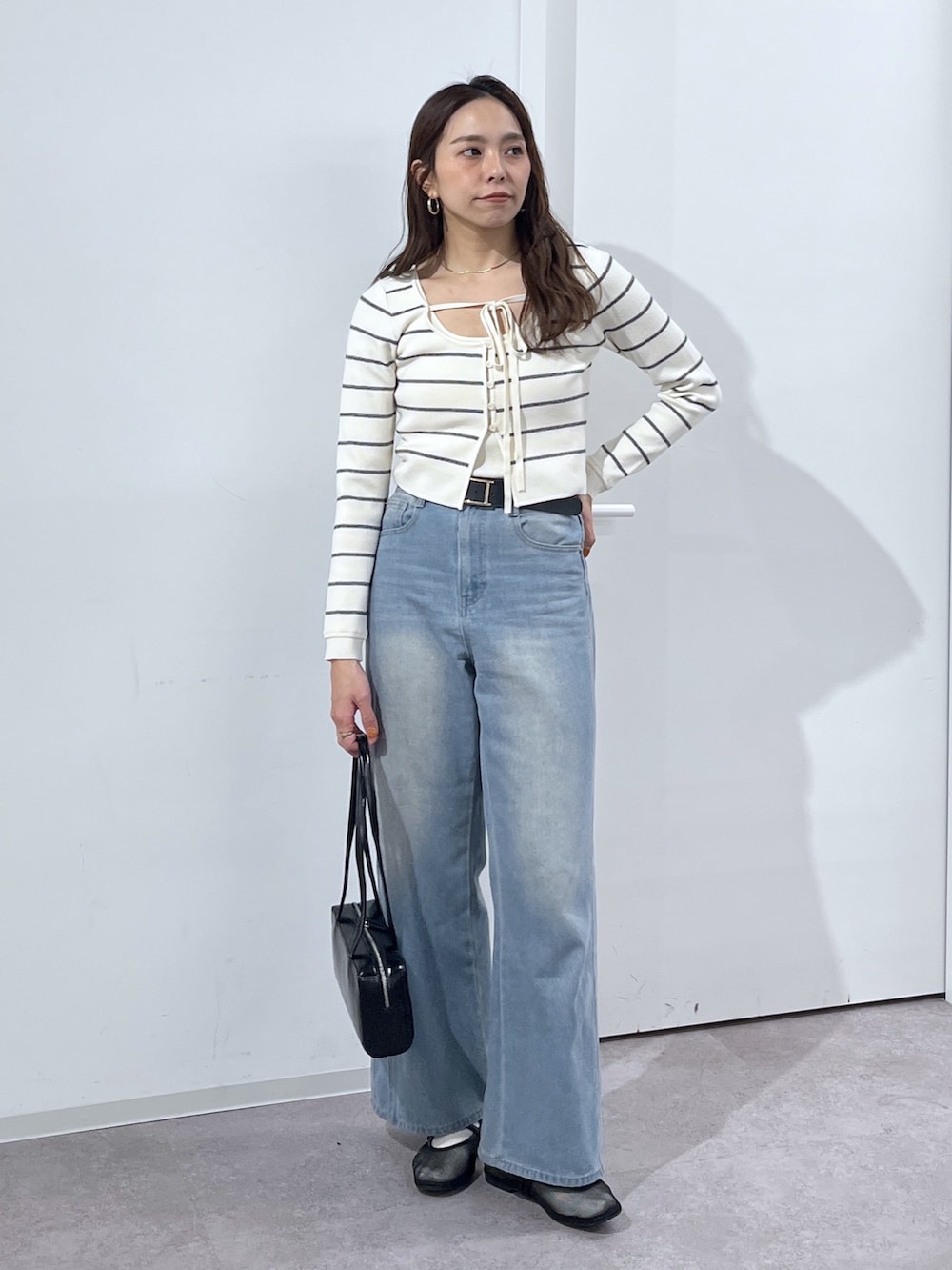 ブラック系のショルダーバッグ、ホワイト系のニット/セーター、ブルー系のデニムパンツを着用したレディースの冬コーディネートの3枚目の写真