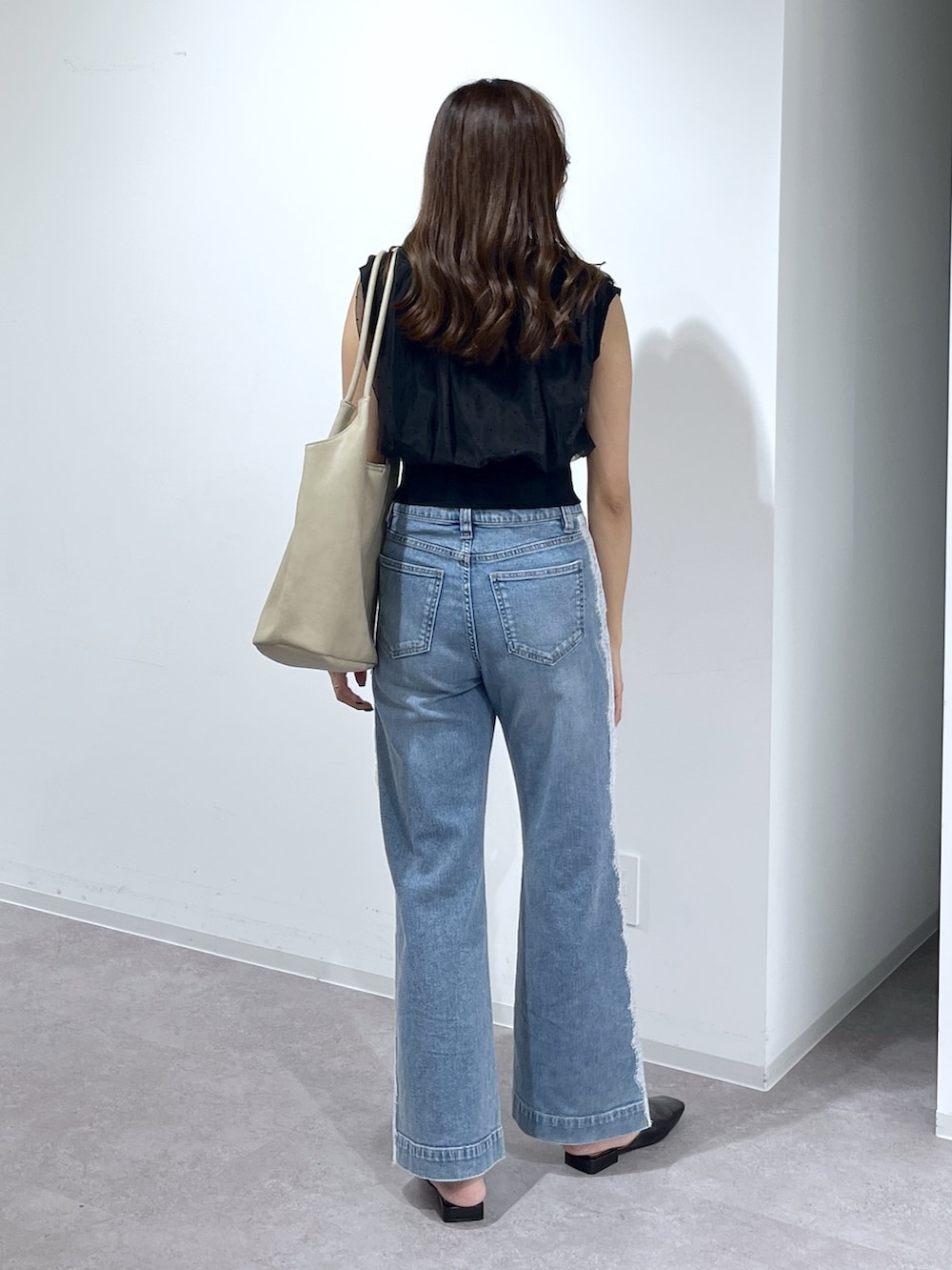 ブラック系のニット/セーター、ブルー系のデニムパンツ、ベージュ系のトートバッグを着用したレディースの夏コーディネートの6枚目の写真