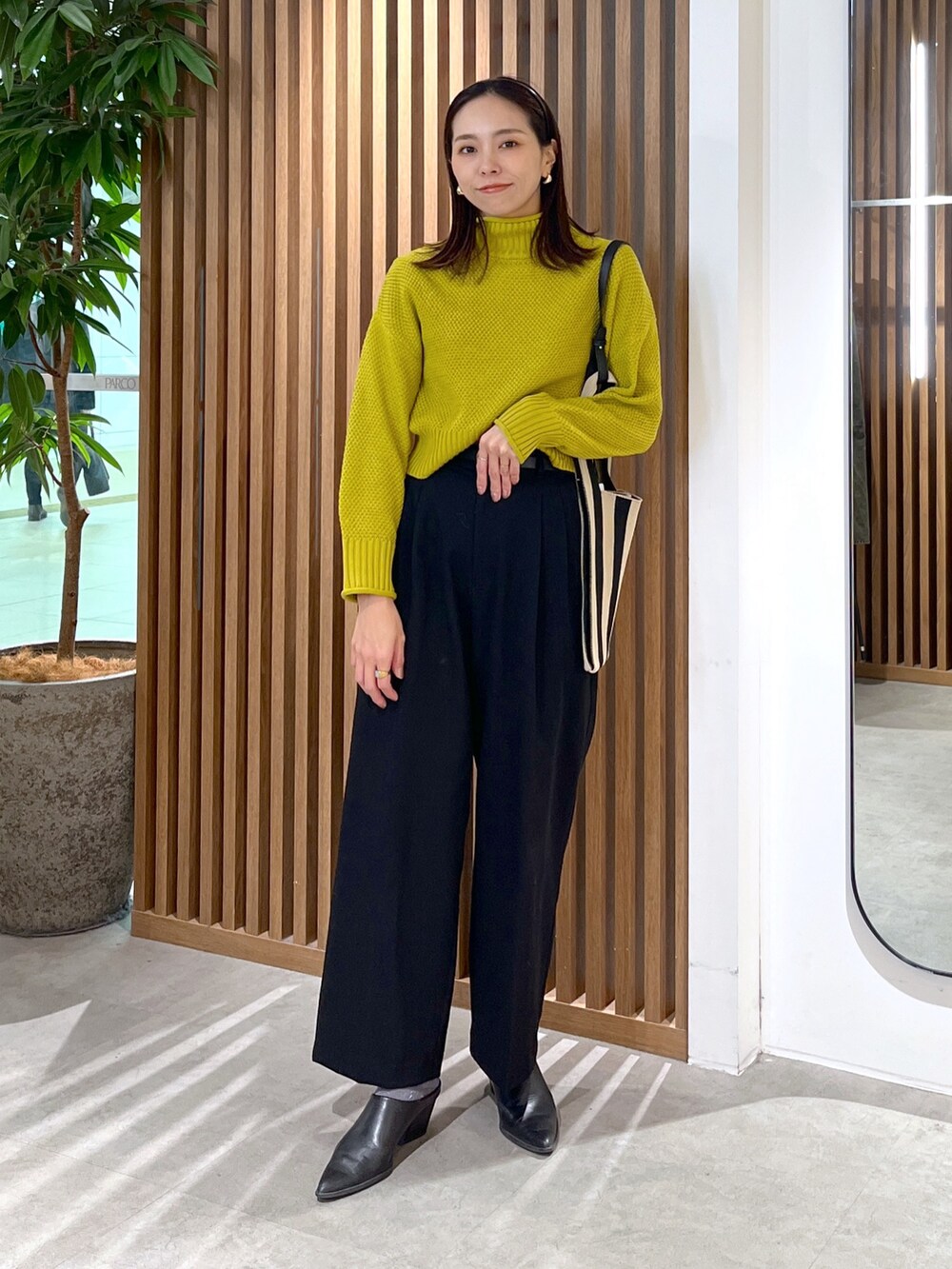 イエロー系のニット/セーター、ブラック系のスラックス、ブラック系のショルダーバッグを着用したレディースの冬コーディネートの2枚目の写真