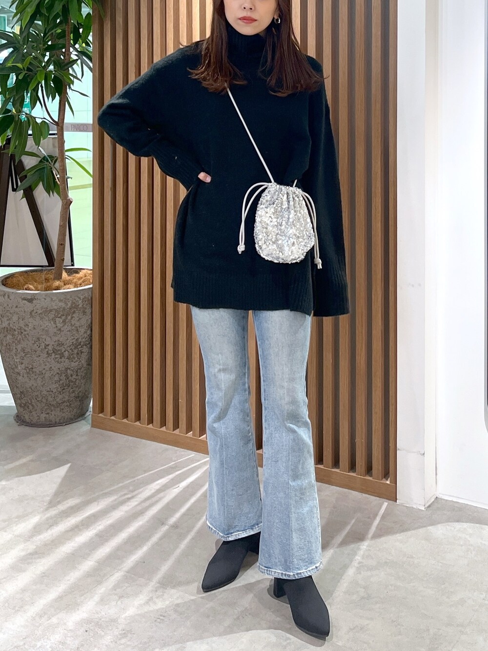 シルバー系のハンドバッグ、ブラック系のニット/セーター、ブルー系のデニムパンツを着用したレディースの冬コーディネートの6枚目の写真